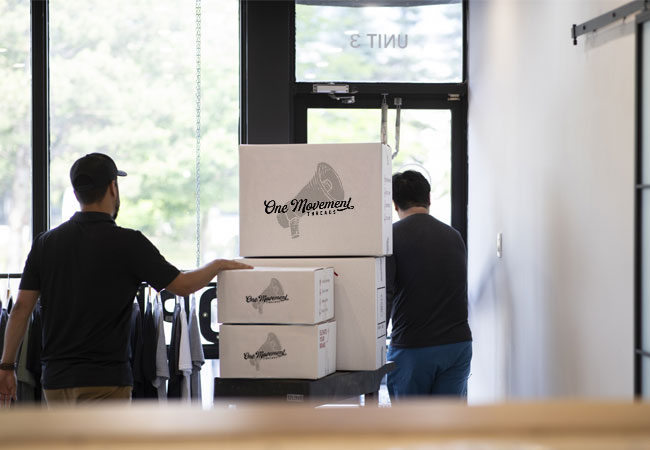 Two people moving One Movement Threads boxes out the door