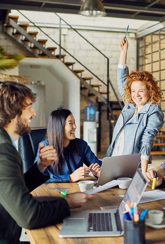 A group of colleagues in a meeting with one lady raising her hand